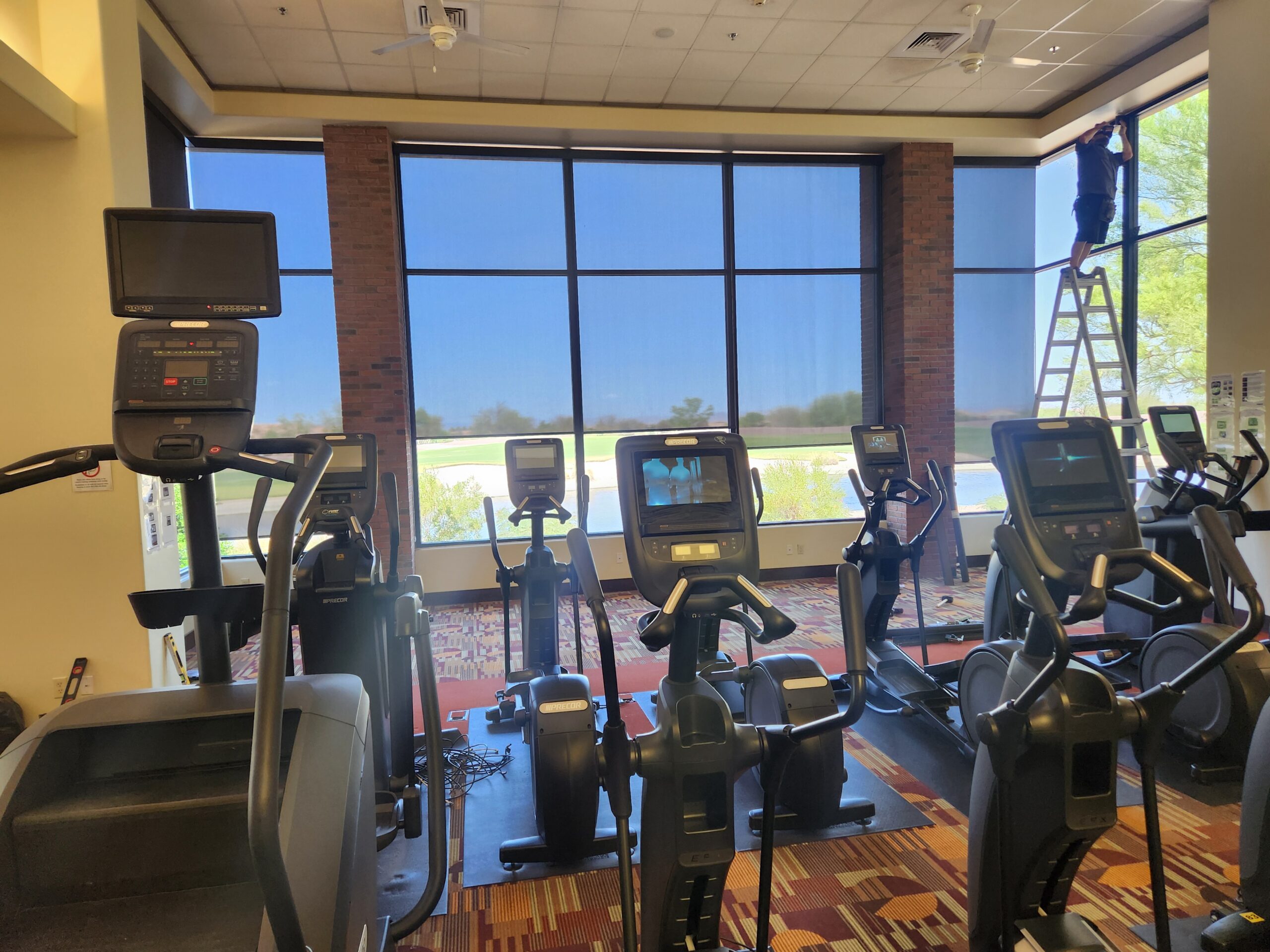 Floor to ceiling gym windows fitted with roller shades to control glare on exercise equipment