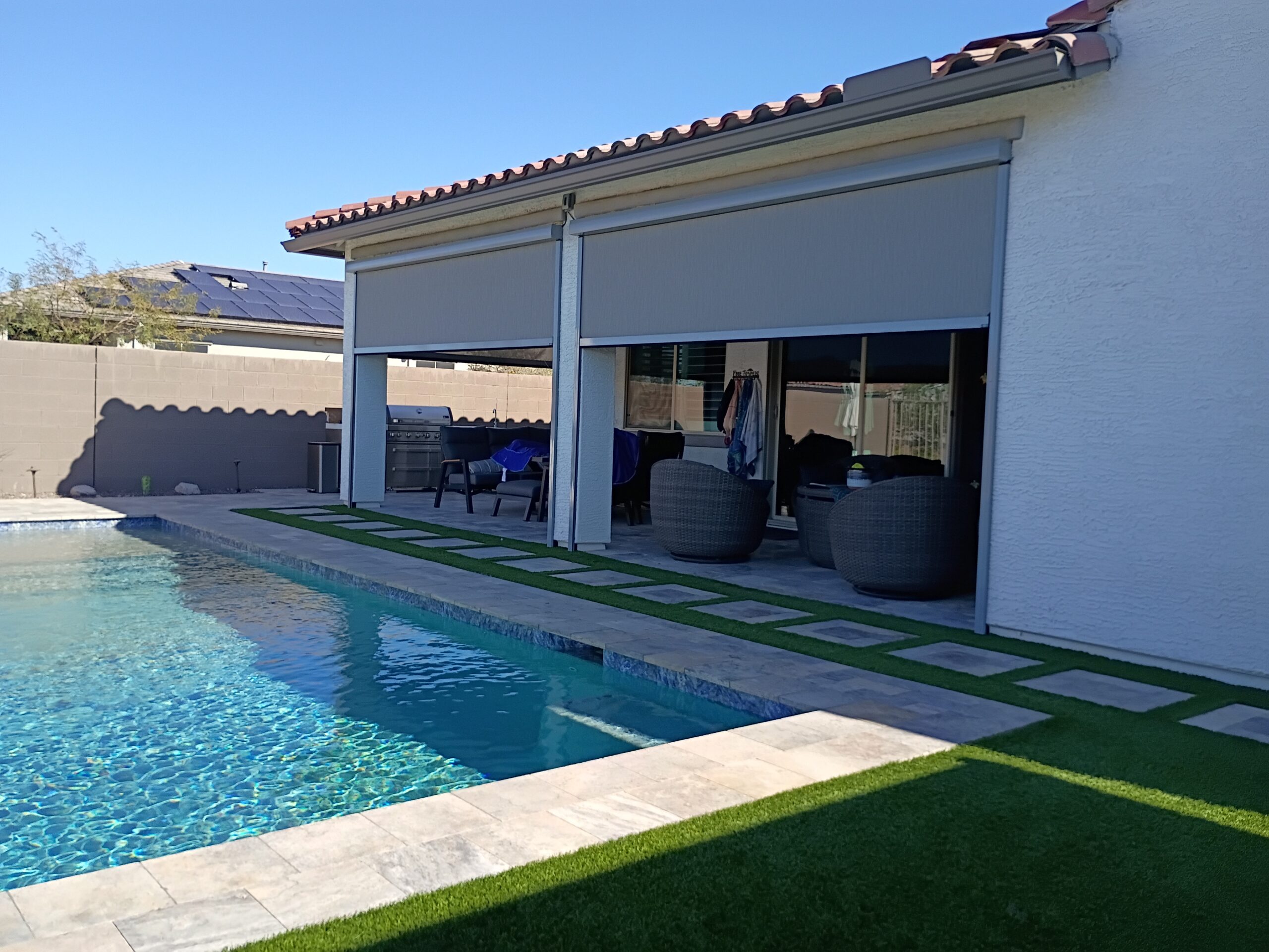 Poolside covered patio with motorized shades lowered along the roofline next to outdoor seating