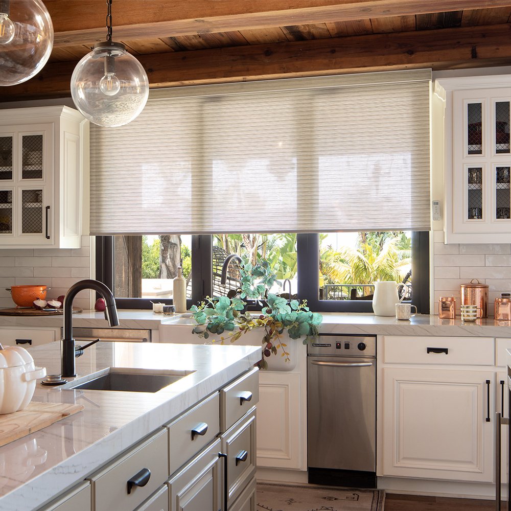 Patterned fabric roller shade lowered over a kitchen window with an island in the foreground